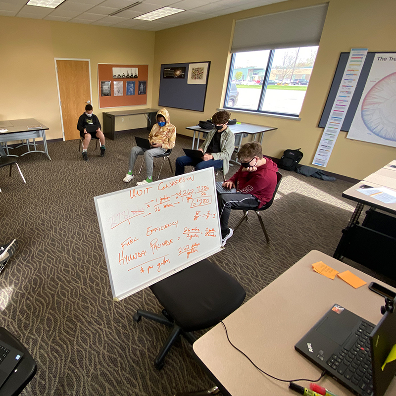 A circle of students in a class with some attending virtually.