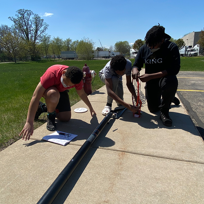 Three students outside assembling a basketball hoop.