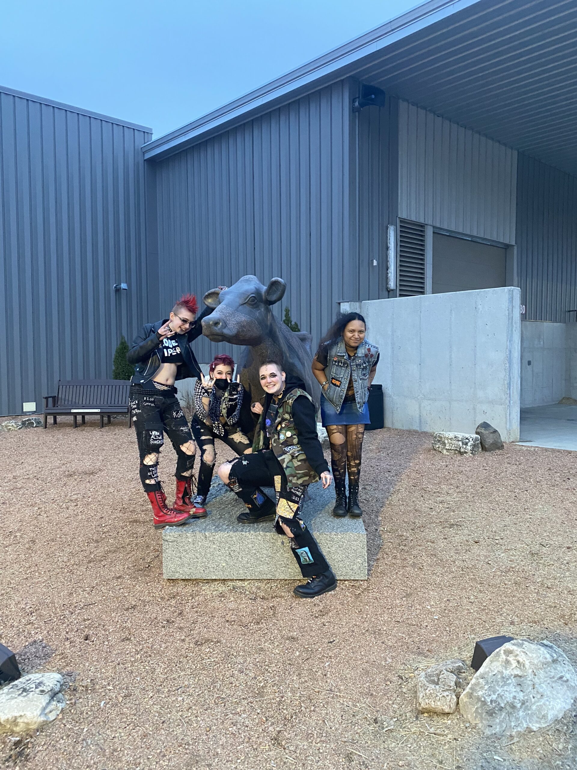 Four Milestone students posing with a cow statue during a student-led outing.