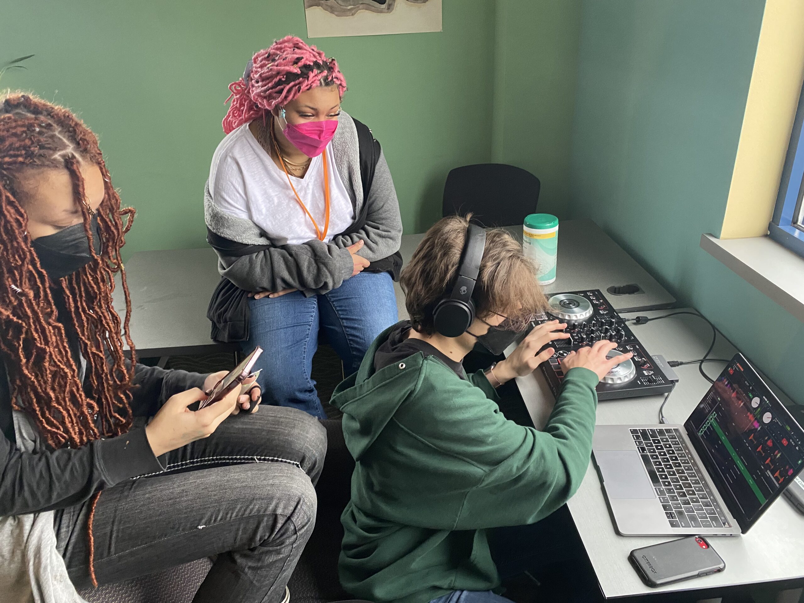 Two students watching as a classmate edits sound files on a laptop.